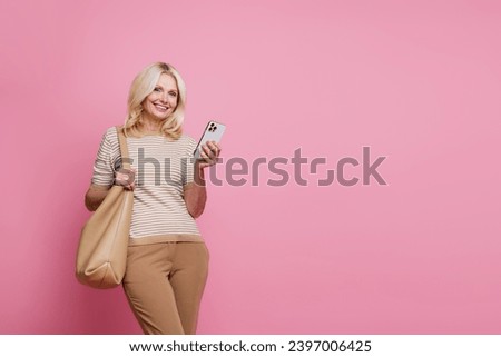 Photo of cheerful grandmother use smart phone texting empty space ad isolated on pink color background