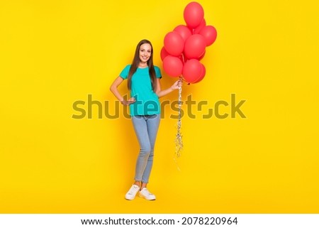 Photo of cheerful guest lady hold bunch balloons wear teal t-shirt jeans sneakers isolated yellow color background