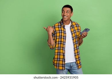 Photo of cheerful guy in yellow plaid shirt pointing finger website he created logo design using phone isolated on green color background - Powered by Shutterstock