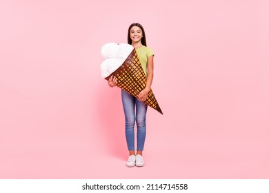 Photo of cheerful hungry little lady hold big cone ice cream wear green top jeans sneakers isolated pink color background