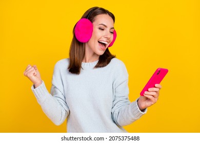 Photo Of Cheerful Joyful Young Woman Wear Ear Warmer Hold Phone Winner Isolated On Yellow Color Background