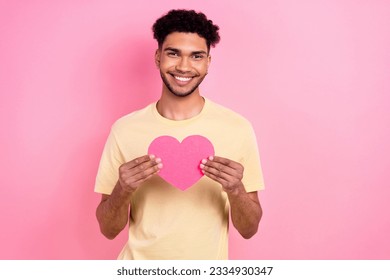 Photo of cheerful kind positive guy wear stylish yellow t-shirt hands hold pink paper postcard heart isolated on pink color background - Shutterstock ID 2334930347