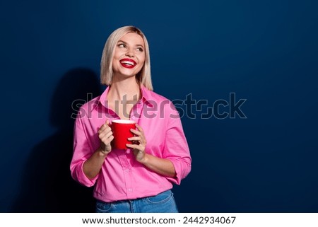 Photo of cheerful lovely girl dressed pink shirt hold cup of coffee look at logo empty space isolated on dark blue color background