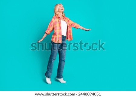 Photo of cheerful lovely pretty retired woman wear checkered stylish clothes look up empty space isolated on cyan color background