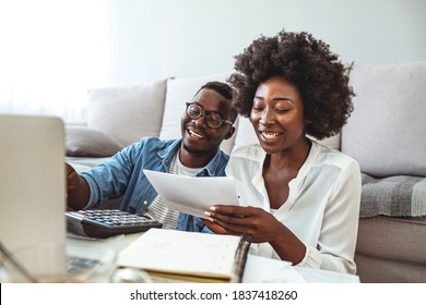 Photo of cheerful loving young couple using laptop and analyzing their finances with documents. Look at papers. Happy couple at home paying bills with laptop
