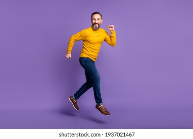 Photo Of Cheerful Man Jump Run Look Camera Wear Yellow Pullover Jeans Footwear Isolated Violet Background