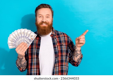 Photo of cheerful man with stylish beard dressed checkered shirt hold money directing empty space isolated on blue color background - Shutterstock ID 2366344033