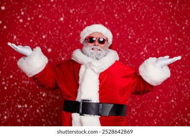 Photo of cheerful man two hands demonstrate empty space variants wear santa hat costume isolated red color background - Powered by Shutterstock