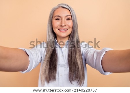Photo of cheerful mature woman shooting selfie vacation trip influencer isolated over beige color background
