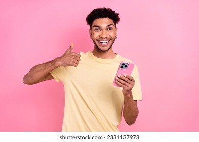Photo of cheerful nice guy afro coiffure dressed yellow t-shirt showing thumb up good job hold phone isolated on pink color background - Shutterstock ID 2331137973