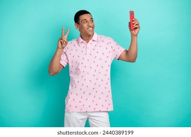 Photo of cheerful nice guy hold smart phone make selfie demonstrate v-sign isolated on teal color background
