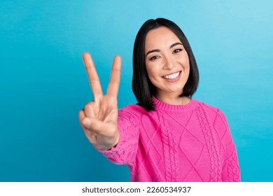 Photo of cheerful nice person beaming smile arm fingers demonstrate v-sign isolated on blue color background