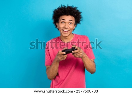 Photo of cheerful optimistic guy with perming coiffure wear pink t-shirt hold playstation joystick isolated on blue color background