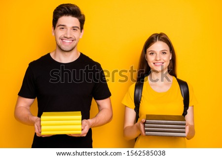 Photo of cheerful positive cute clever nice groupmates holding tutorials in their hands wearing black t-shirt smiling toothily isolated over vibrant shine yellow color background