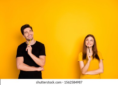 Photo of cheerful positive cute nice charming pretty couple holding pens wearing black t-shirt smiling toothily looking into empty space a fit of thoughts isolated over bright shiny color background