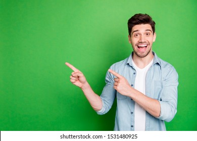 Photo of cheerful positive handsome man pointing at empty space expressing ecstatic emotions on face with bristle isolated over green vivid color background