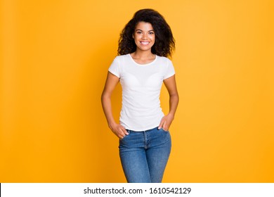 Photo of cheerful positive nice cute girlfriend with hands in pocket standing confidently in white t-shirt isolated over vivid color background in jeans denim
