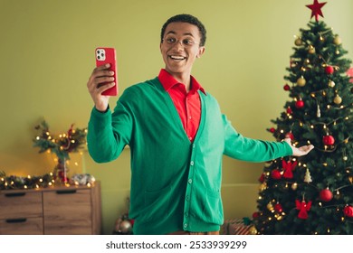 Photo of cheerful positive nice young man wearing green cardigan showing xmas pine tree new year time decorations indoors room - Powered by Shutterstock