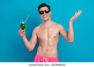 Photo of cheerful positive young guy topless dark eyewear smiling drinking cocktail isolated blue color background
