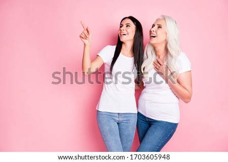 Photo of cheerful pretty aged mother young daughter ladies spend time together see funny guys direct finger laughing wear white t-shirts jeans isolated pastel pink color background