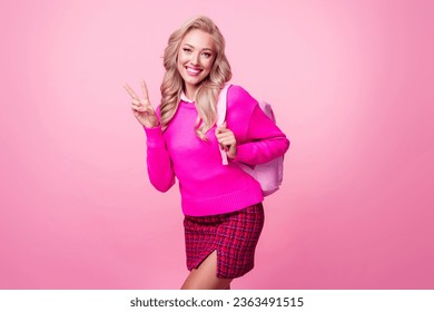 Photo of cheerful pretty girl wear trendy pullover mini skirt hold rucksack demonstrate v-sign isolated on pink color background
