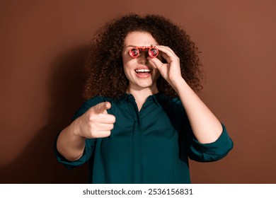 Photo of cheerful pretty lady dressed green shirt looking binoculars empty space isolated brown color background - Powered by Shutterstock