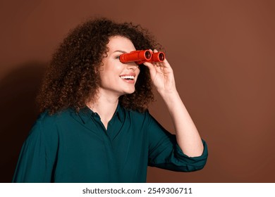 Photo of cheerful pretty lady dressed green shirt looking binoculars empty space isolated brown color background - Powered by Shutterstock