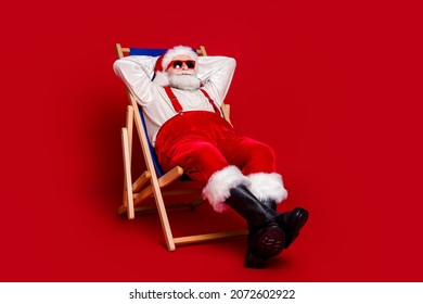 Photo of cheerful pretty retired man wear santa claus costume smiling sitting deckchair arms behind head isolated red color background - Powered by Shutterstock