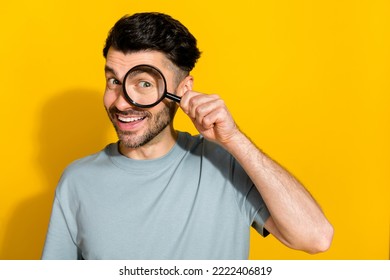 Photo of cheerful satisfied man stylish clothes using magnifying glass find investigation empty space isolated on yellow color background