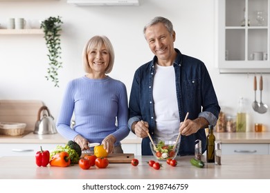 Photo Of Cheerful Senior Man And Woman Cooking Together At Home, Making Delicious Vegetable Salad, Smiling At Camera, Kitchen Interior, Copy Space. Healthy Diet For Elderly People