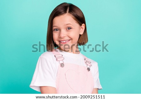 Photo of cheerful shiny schoolgirl dressed pink overall smiling isolated turquoise color background