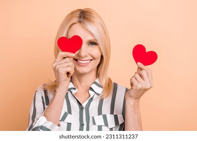 Photo of cheerful sweet person hold small red paper hearts cover one eye isolated on beige color background - Shutterstock ID 2311311237