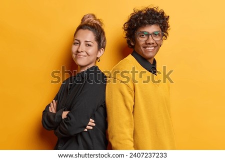 Photo of cheerful woman and man stand backs with folded arms feel happy and self confident dressed in casual clothing smile satisfied isolated on yellow background. Friendly team collaborate together