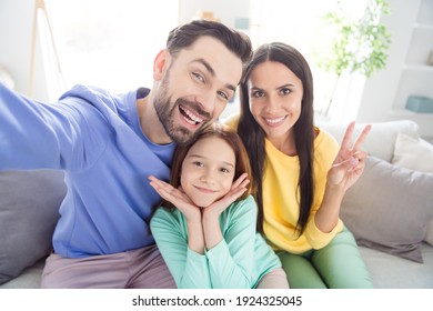 Photo Of Cheerful Young Family Mom Dad Daughter Happy Positive Smile Show Peace Cool V-sign Sit Sofa Home