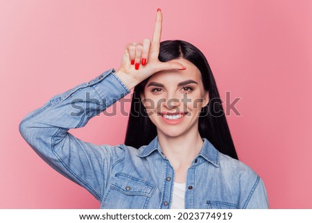 Photo of cheerful young girl makes loser gesture mocking at someone isolated over purple background