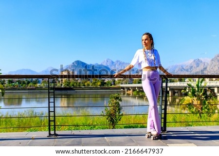 Photo of cheerful young happy woman wear white t-shirt and bell-bottomed trousers with pink pastel color roller skates outdoors in sunny day