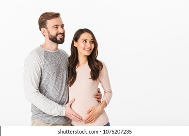 Photo of cheerful young man standing with his pregnant woman isolated over white background wall. Looking aside.