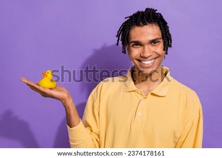 Photo of cheerful youngster guy wear yellow stylish shirt holding hand his favorite rubber duck toy isolated on purple color background