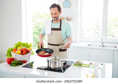 Foto del chef un hombre apuesto y maduro sostiene carne de pan frita vestida con una camiseta azul delantal cocina en casa en el interior