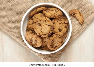 A photo of chocolate chips cookies in a bowl, shot from above on a burlap and light wooden background texture, with copyspace - Powered by Shutterstock