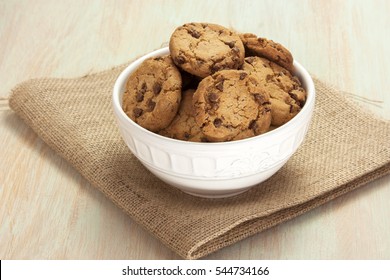 A photo of chocolate chips cookies in a bowl, shot on a burlap and light wooden background texture, with copyspace - Powered by Shutterstock