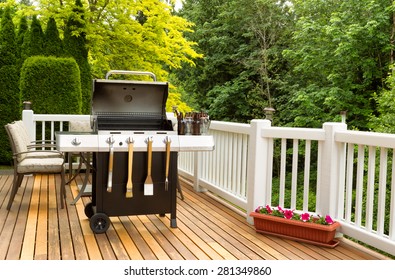 Photo of a clean barbecue cooker with cookware and cold beer in bucket on cedar wood patio. Table and colorful trees in background. 