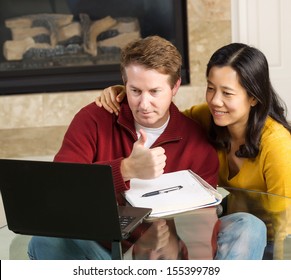 Photo Of Close Mature Couple Looking At Information, Man Giving Thumbs Up, On The Computer Screen Together With Fireplace In Background  