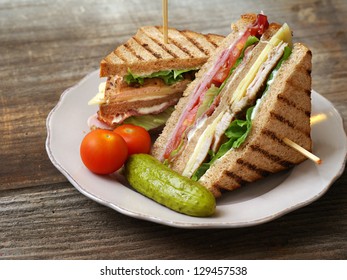 Photo of a club sandwich made with turkey, bacon, ham, tomato, cheese, lettuce, and garnished with a pickle and two cherry tomatoes. - Shutterstock ID 129457538