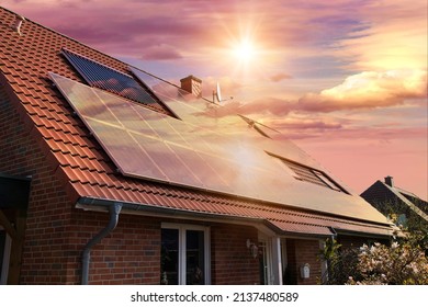 Fotocollage von Solarzellen, Fotovoltaik auf dem roten Dach eines Hauses und ein schöner Himmel mit der untergehenden Sonne. Alternative Stromquelle. Konzept der nachhaltigen Ressourcen