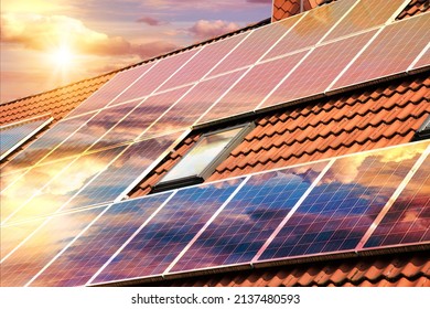 Photo collage of solar panels, photovoltaics on the red roof of a house and a beautiful sky with the setting sun. Alternative electricity source. Concept of sustainable resources
