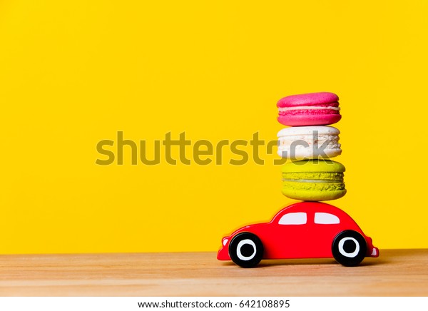 photo of colorful macaroons and car\
shaped toy on the wonderful yellow studio\
background