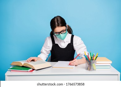 Photo of concentrated high school girl sit table prepare graduate exam study covid remote write note book wear medical mask white blouse black overall uniform isolated blue color background