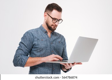 Photo of concentrated young bearded man wearing glasses dressed in shirt using laptop isolated over white background.