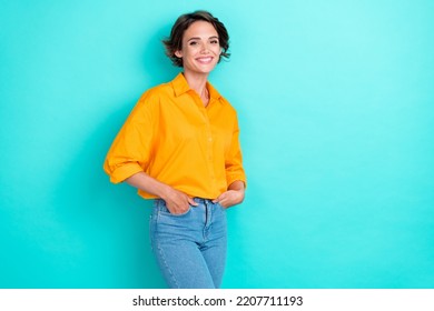 Photo of confident adorable woman bob hairstyle wear yellow blouse denim jeans arms in pockets isolated on turquoise color background